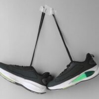 Stylish black and green running shoes creatively hung on a grey wall, showcasing modern design.