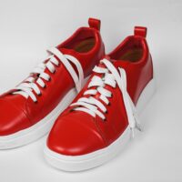 Pair of stylish red sneakers with white laces on a white surface.