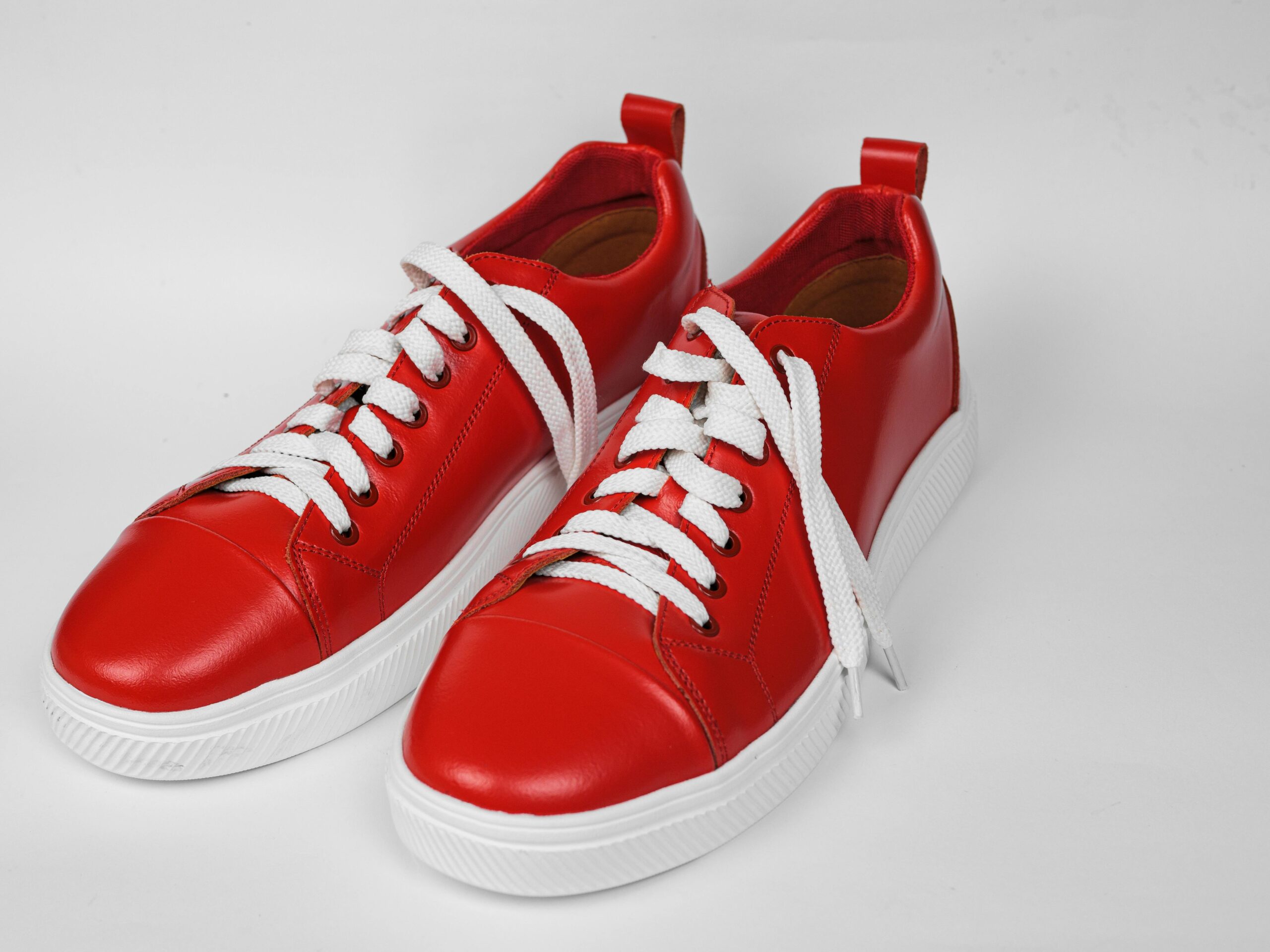 Pair of stylish red sneakers with white laces on a white surface.